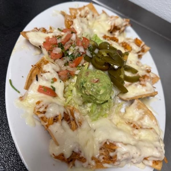 Los Charros nachos with melted cheese, pico de gallo, guacamole, and jalapeños on a white plate.