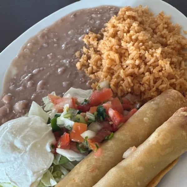 A plate of Mexican food with two taquitos, refried beans, rice, pico de gallo, and sour cream.