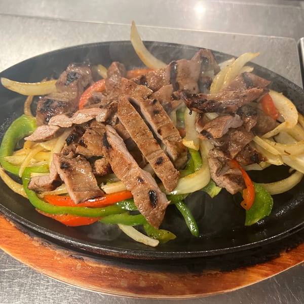 Sizzling Los Charros fajitas with grilled steak, onions, and colorful bell peppers on a hot plate.