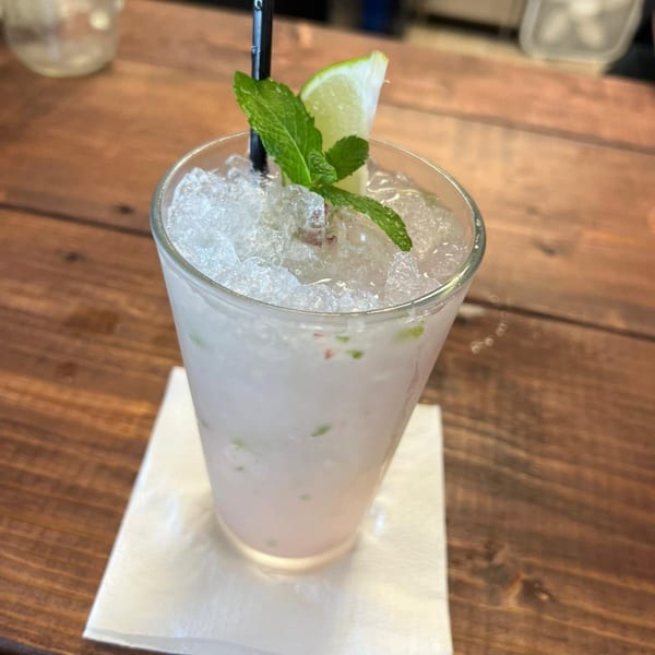 A refreshing mojito with crushed ice, mint, and a lime wedge on a wooden table.