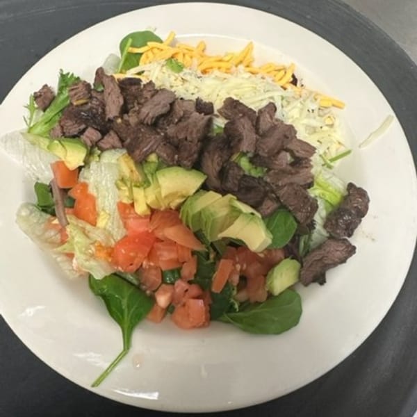 A Los Charros Mexican steak salad with avocado, tomatoes, lettuce, and shredded cheese.