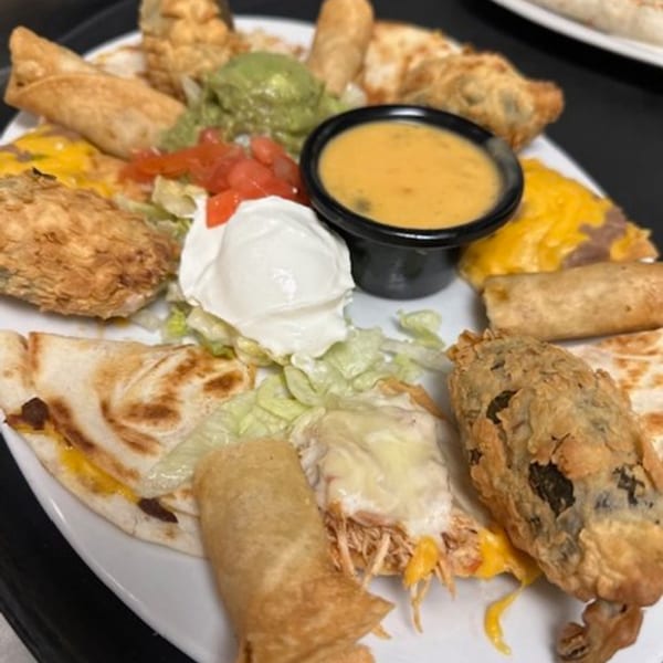 A large platter of Los Charros Mexican appetizers including taquitos, quesadillas, and fried items with dips.