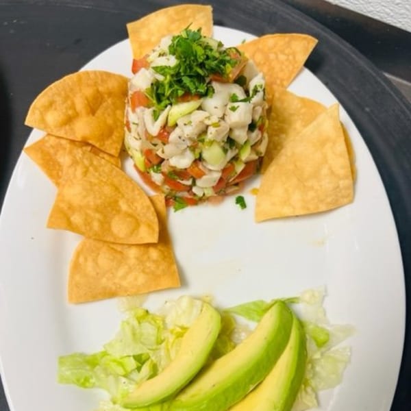 Los Charros' ceviche with tortilla chips, lettuce, and avocado slices on a white plate.