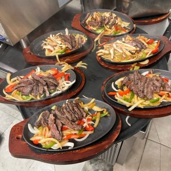 Six sizzling fajita platters with steak, onions, and bell peppers on a rotating stand.