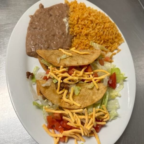 Two crispy tacos with lettuce, tomatoes, and shredded cheese, served with refried beans and rice.