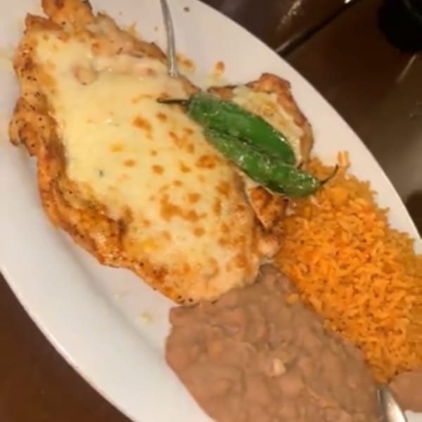 Cheesy chicken breast with two green peppers, orange rice, and refried beans on a white plate.