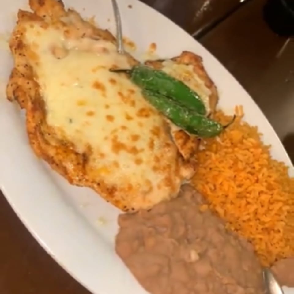 Cheesy chicken breast with two green peppers, orange rice, and refried beans on a white plate.