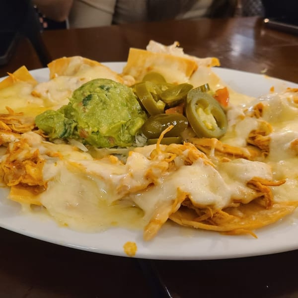 Los Charros' chicken nachos with melted cheese, guacamole, and sliced jalapeños on a white plate.