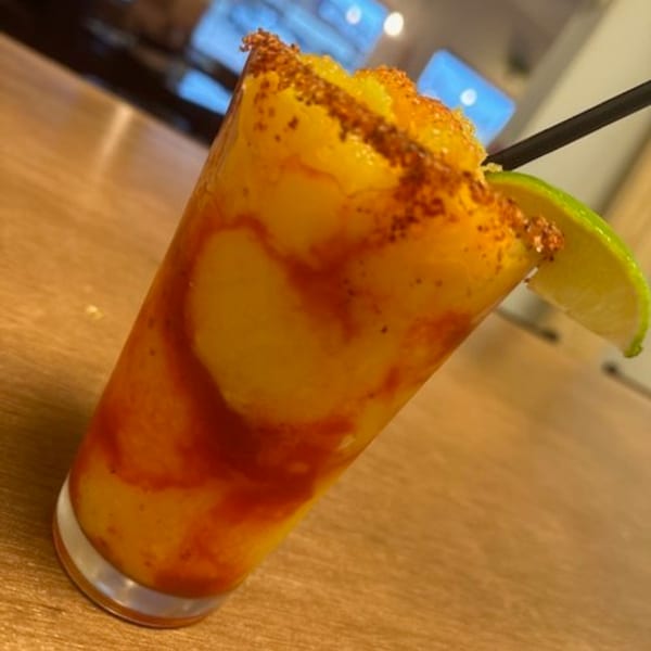 A vibrant mango chamoy margarita with a chili-lime rim and a lime wedge, on a wooden table.