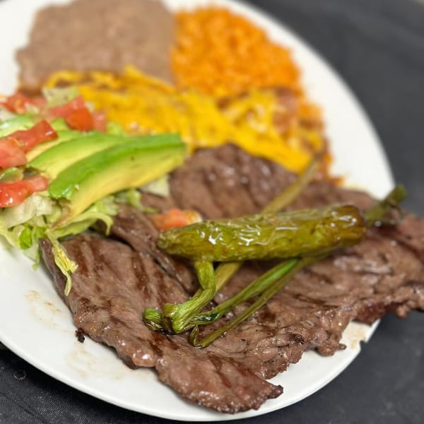 Grilled steak with a roasted green chili, avocado, lettuce, tomatoes, rice, and refried beans.