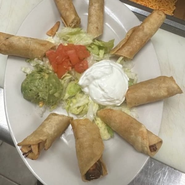Los Charros' taquitos arranged on a plate with shredded lettuce, diced tomatoes, guacamole, and sour cream.