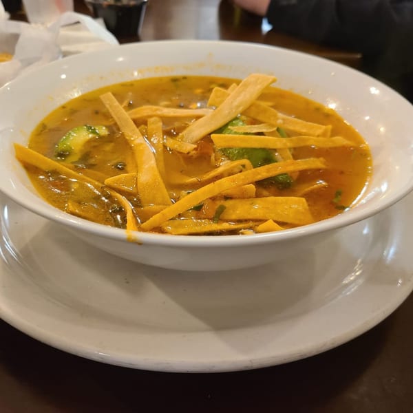 A bowl of Los Charros tortilla soup with avocado slices and tortilla strips.
