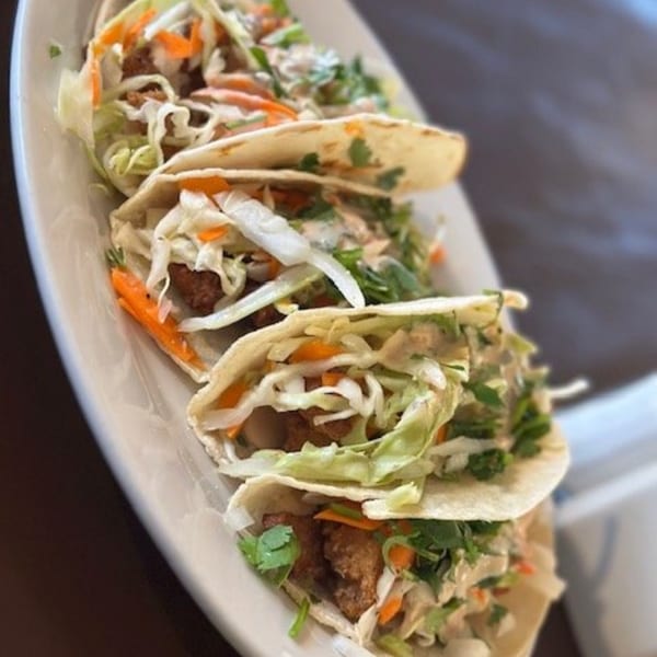 Four Los Charros fish tacos with cabbage, carrots, and cilantro on a white plate.