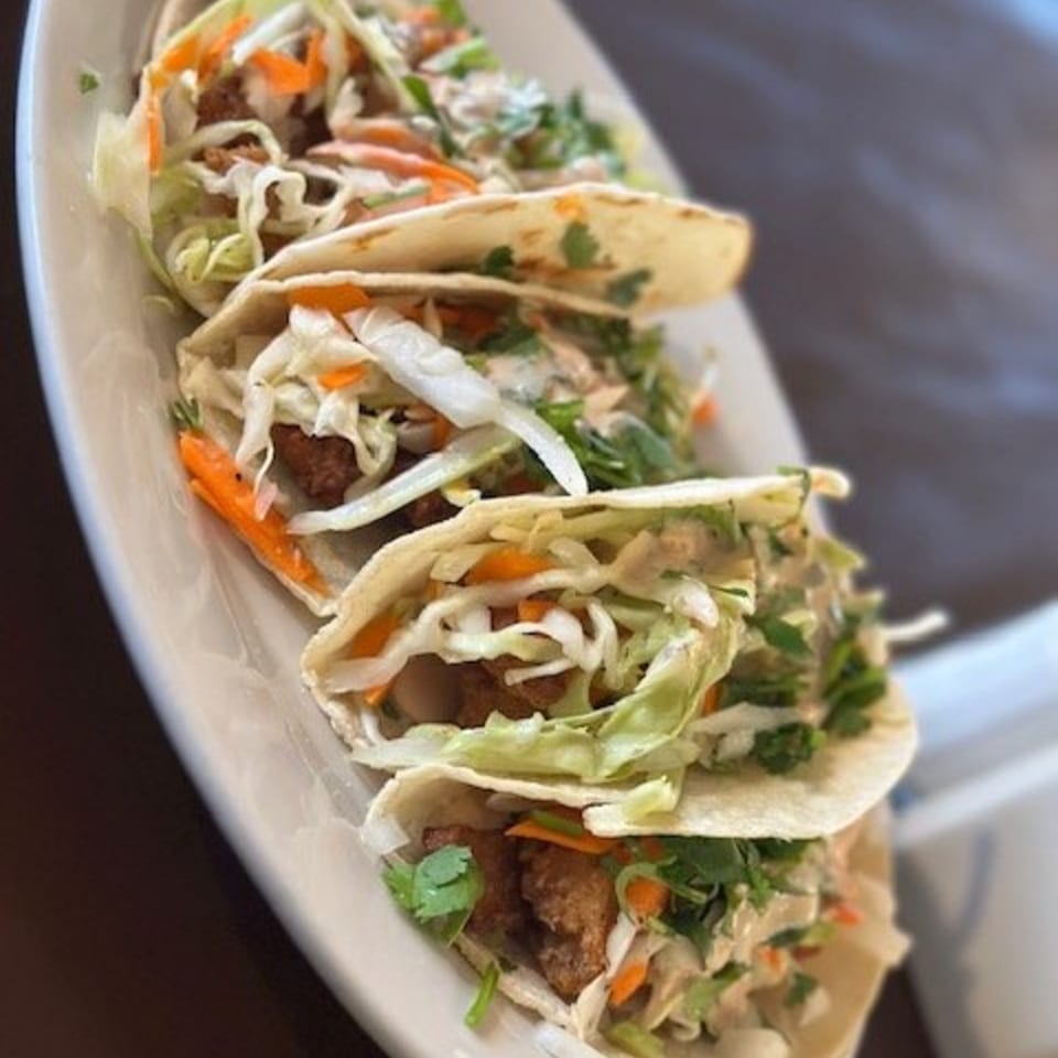 Four Los Charros fish tacos with cabbage, carrots, and cilantro on a white plate.