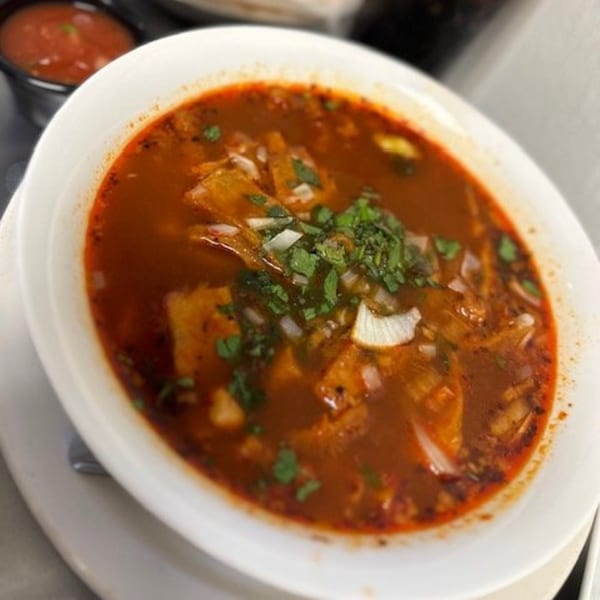A bowl of Los Charros' red Mexican soup, garnished with chopped onions and cilantro.