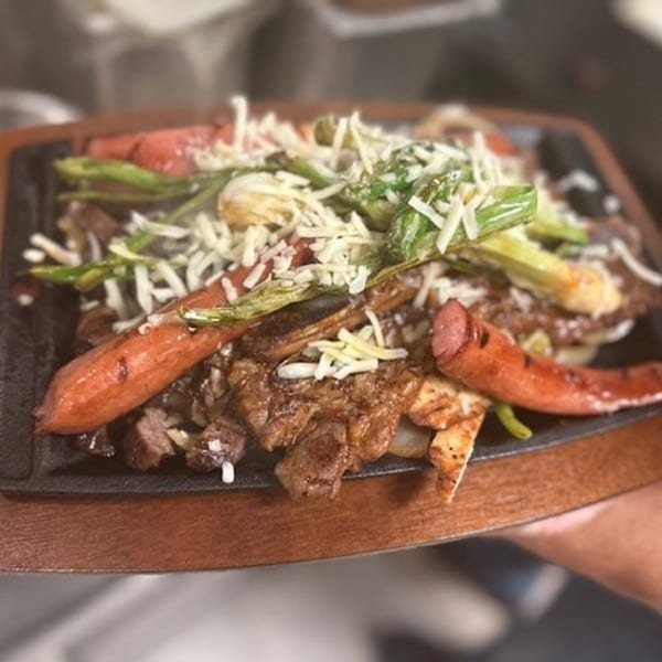 Sizzling Mexican fajita platter with steak, sausage, green peppers, and melted cheese.