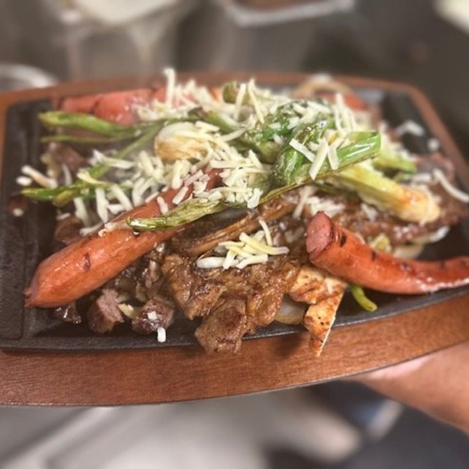 Sizzling Mexican fajita platter with steak, sausage, green peppers, and melted cheese.
