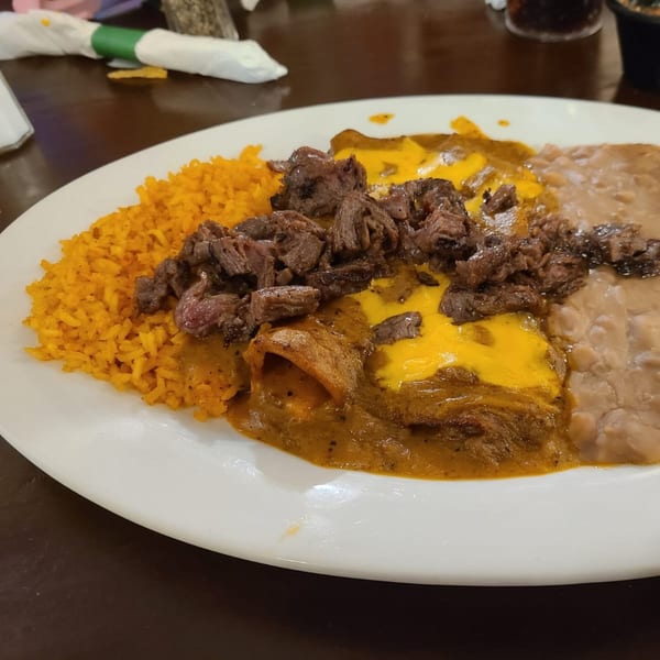 A Los Charros Mexican dish with enchiladas, rice, beans, and carne asada on a white plate.