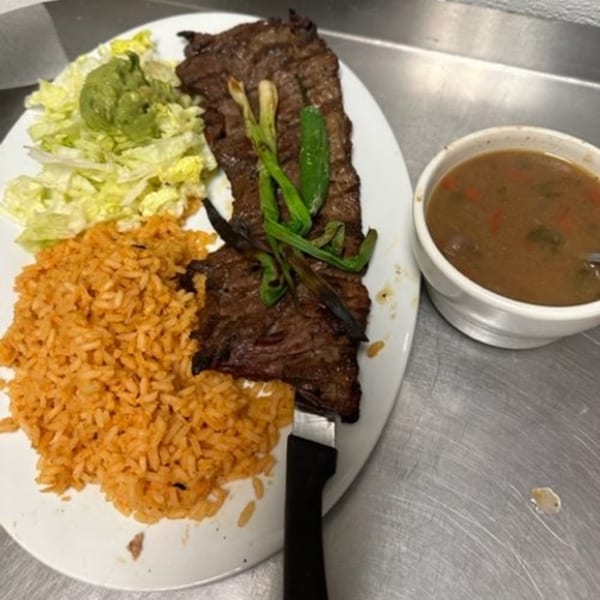 Los Charros' carne asada with rice, lettuce, guacamole, grilled green onions, and a side of soup.
