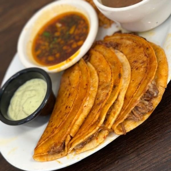 Los Charros birria tacos with consome and a side of green sauce on a white plate.