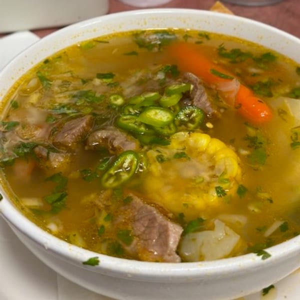 Close-up of a bowl of Los Charros Mexican beef soup with corn, carrots, and green chilies.