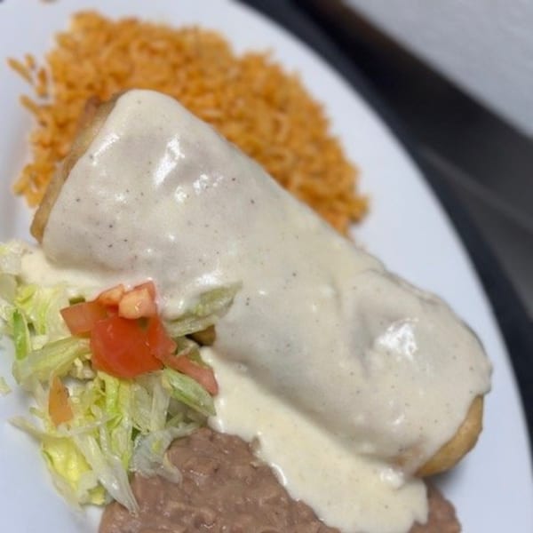 A chimichanga covered in white sauce, served with rice, refried beans, and a side salad.