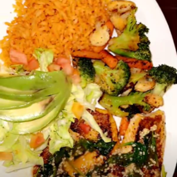 A Mexican dish with orange rice, grilled vegetables, avocado slices, and a side salad.